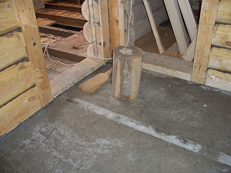На фото показано бетонное основание пола в бревенчатом срубе.